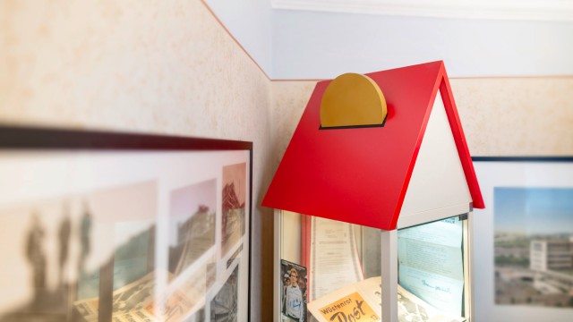 Fotografie eines Modellhauses mit Glaskorpus, darin zu sehen ist eine alte Printausgabe der Wüstenrot Post